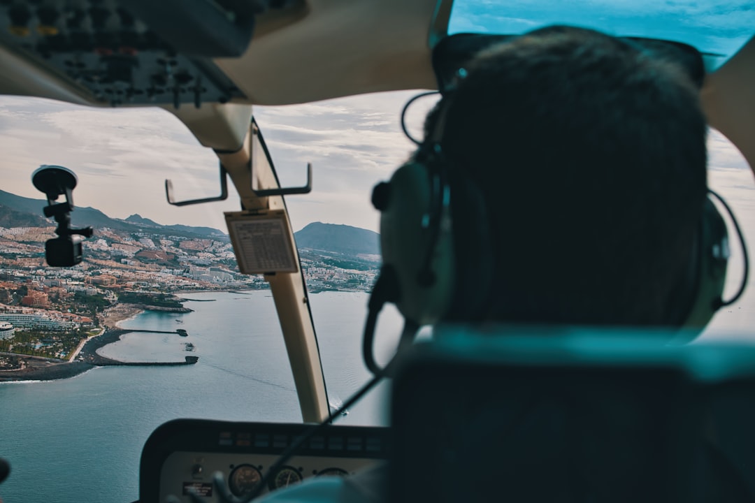 a man flying a helicopter over a large body of water, Flying a helicopter is an exhilarating experience! The freedom and