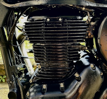 Close-up view of a black motorcycle engine with visible fins and bolts, highlighting the intricate mechanical details and metallic texture.