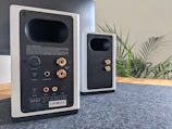 A pair of modern bookshelf speakers placed on a wooden stand.