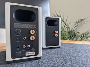 A pair of modern bookshelf speakers placed on a wooden stand.