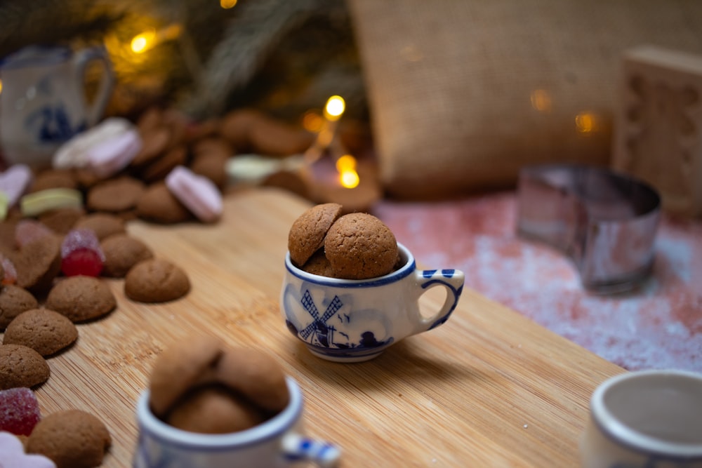 a wooden table topped with two mugs filled with cookies