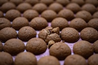 Multiple round, brown cookies are arranged in a grid pattern. One cookie in the center is broken into pieces, revealing the crumbs inside.