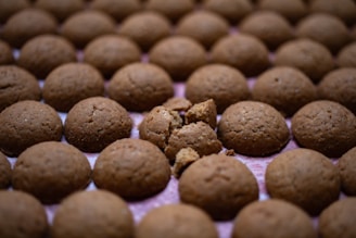 Multiple round, brown cookies are arranged in a grid pattern. One cookie in the center is broken into pieces, revealing the crumbs inside.