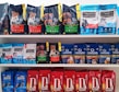 A variety of dog food bags arranged on shelves. The top shelf displays brands such as Cibau and Formula Natural with packaging in black, green, and blue colors. The middle shelf includes Formula Natural and Origens with a mix of blue and red packages. The bottom shelf features Daldog with red packaging.