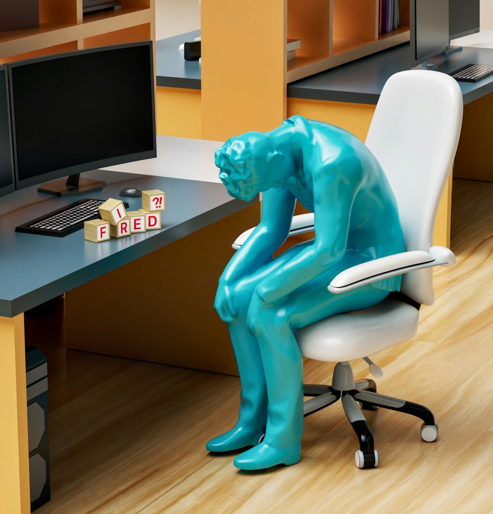 une statue d’une personne assise sur une chaise devant un ordinateur