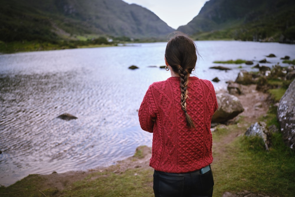 a woman in a red sweater looking at a lake