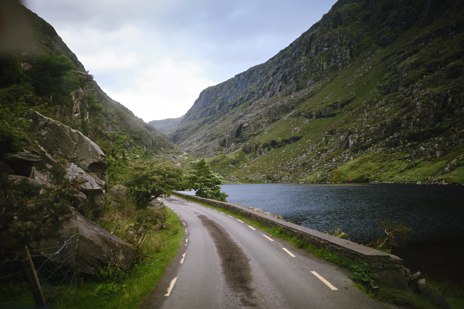 Car following a narrow road between an Irish lake and mountain