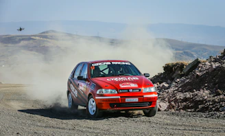 A dynamic shot of a rally car kicking up dust on a rugged Indian terrain during a high-speed race.