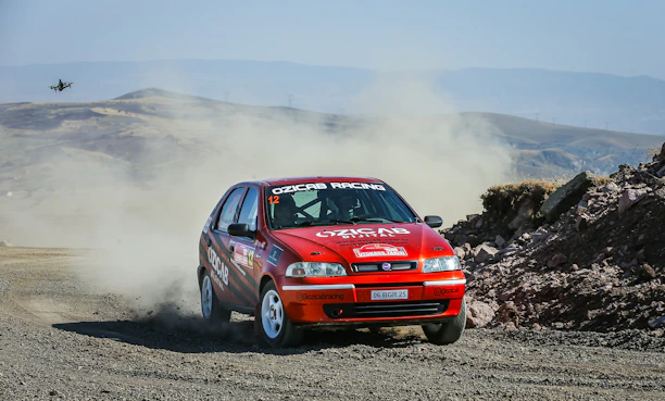 A dynamic shot of a rally car kicking up dust on a rugged Indian terrain during a high-speed race.