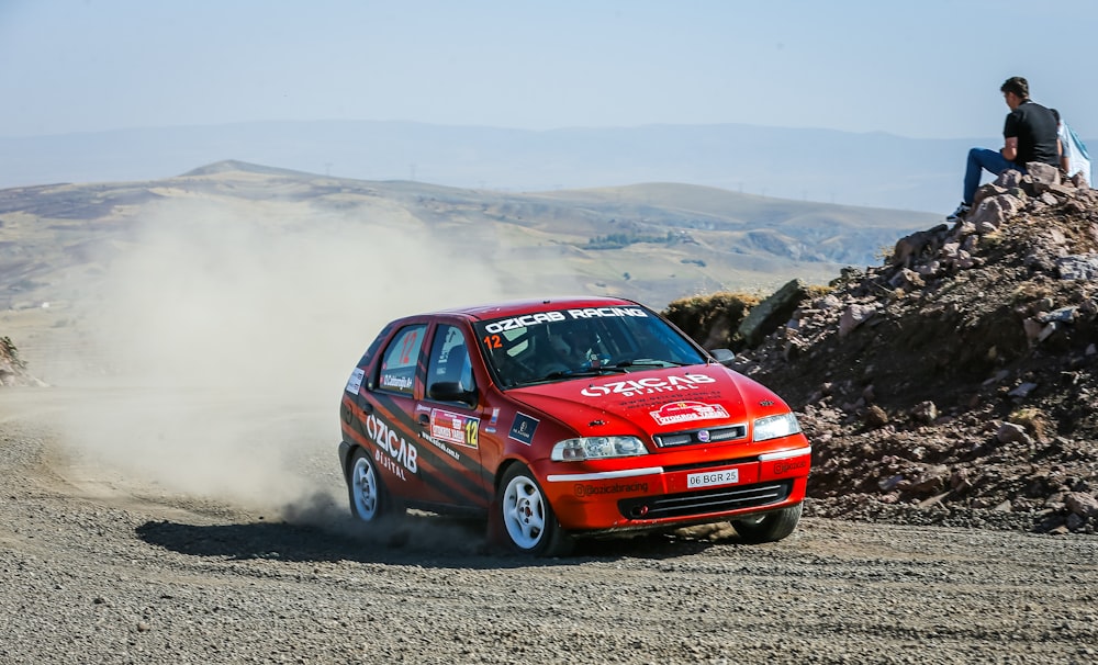 a small red car driving down a dirt road