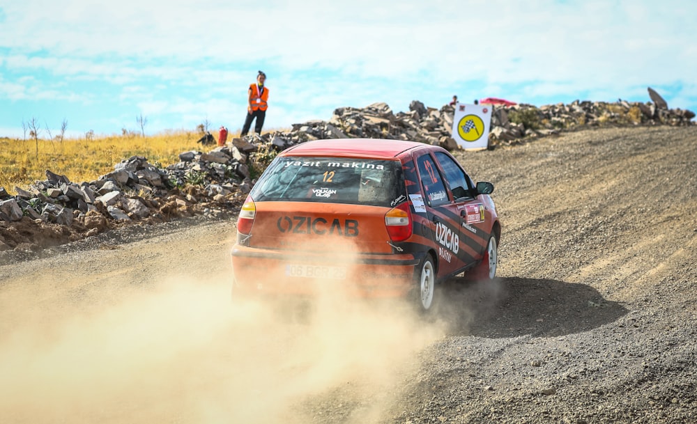 a red car driving down a dirt road