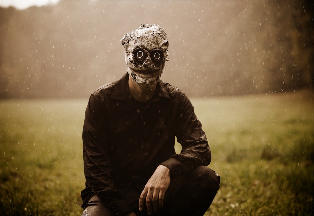 a man wearing a mask sitting in a field