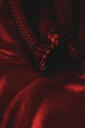 A pair of legs wearing fishnet stockings is resting on a red textured fabric, creating a shadowy and moody atmosphere with the dim lighting.