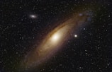 A stunning view of a spiral galaxy with a bright central core surrounded by swirling arms. Countless stars are scattered across the dark background, some forming clusters or appearing as bright points of light.