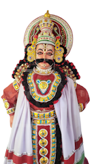 A traditional Yakshagana dancer wearing an elaborate costume with intricate beadwork and colorful embellishments. The headgear is ornate with a detailed design, featuring vibrant reds, yellows, and blues. Facial makeup is distinctive with striking lines and patterns.