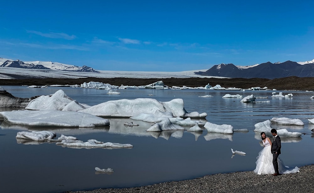 um noivo parado na margem de um lago cercado por icebergs