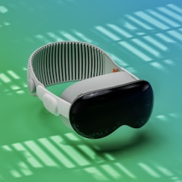 A sleek virtual reality headset with a dark visor and adjustable white strap is placed against a gradient background of green and blue shades. The lighting creates patterns of shadows and highlights that add a dynamic effect.