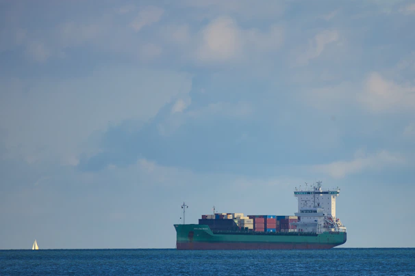 Cargo ship loaded with containers sailing under a clear blue sky.