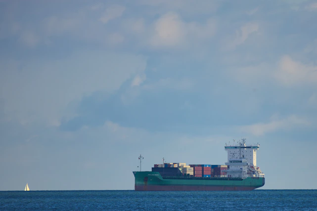 A cargo ship loaded with containers sailing under a clear sky, symbolizing international trade.