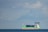A large cargo ship loaded with containers sailing on the ocean under a clear sky.