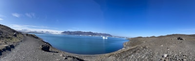 A panoramic view of the Rocky Mountains with a crystal-clear lake reflecting the peaks under a bright blue sky.