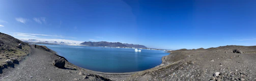 A panoramic shot of Mangla Lake shimmering under a clear blue sky, as seen from Peer Gali.