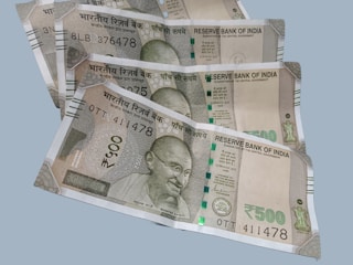 A collection of multiple Indian 500 rupee banknotes fanned out on a flat surface. Each note features a portrait of Mahatma Gandhi and includes text in both Hindi and English. The currency includes security features such as a security thread and watermark.