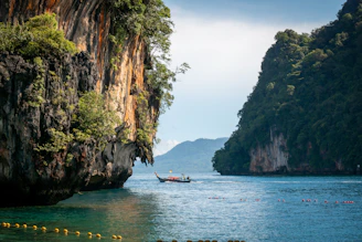 A serene boat gliding through the emerald waters of Phang Nga Bay, limestone cliffs towering nearby.