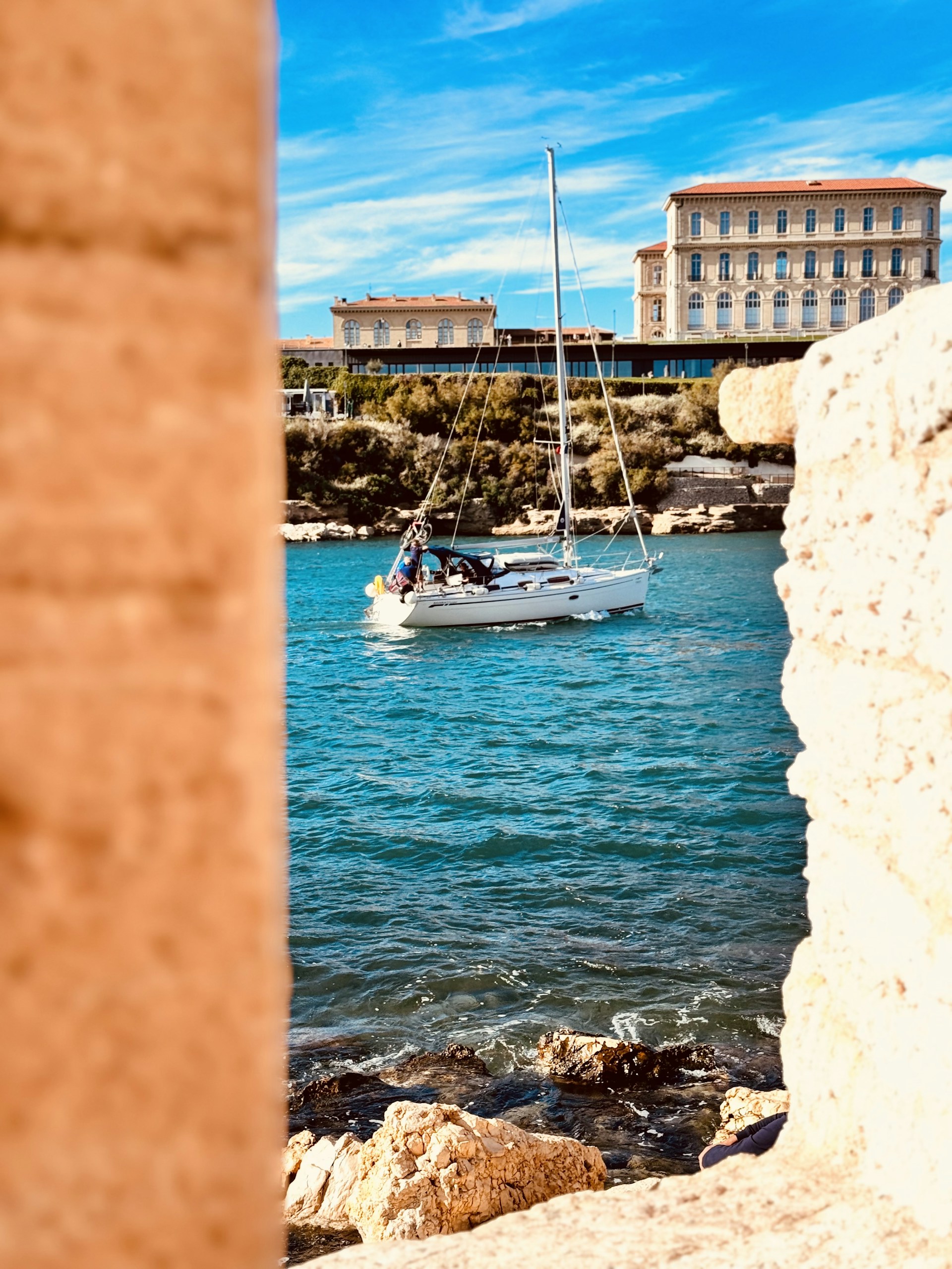 A vibrant sailboat with colorful sails gliding past rocky coastal cliffs on a sunny day.