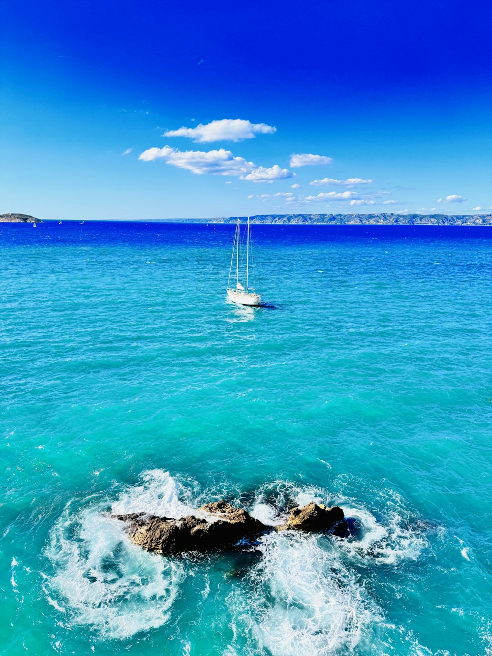 a sailboat in the ocean with a rock in the foreground