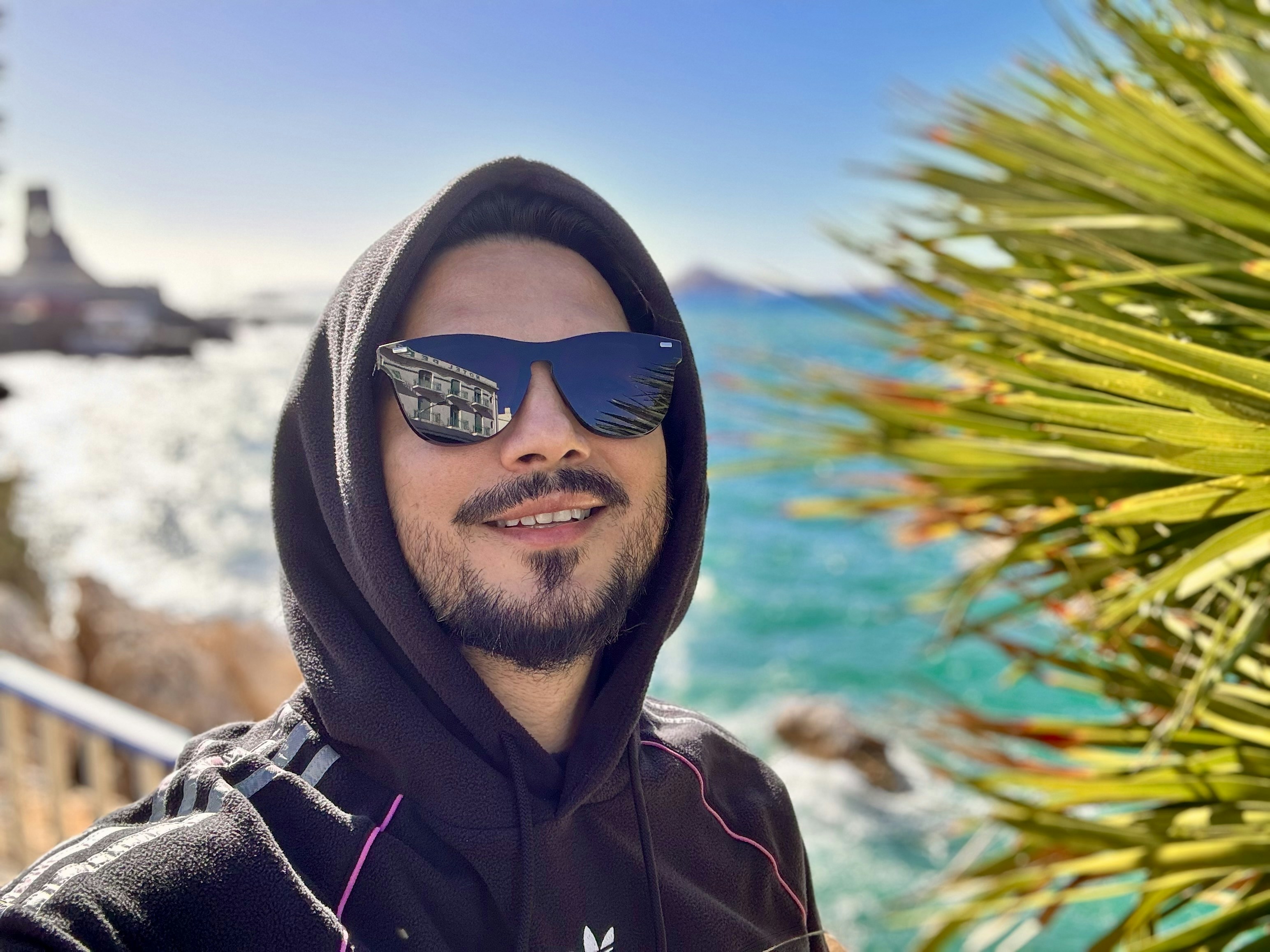 a man wearing a hoodie and sunglasses standing in front of the ocean