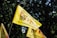 Yellow flags with text in multiple languages featuring a logo with a silhouette, against a backdrop of dark green trees.