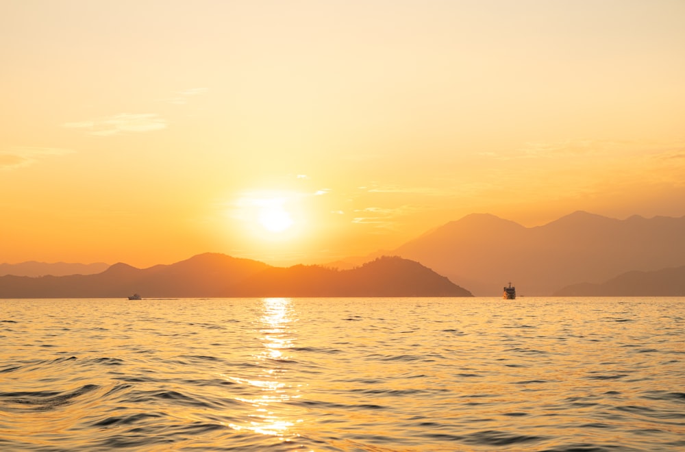 the sun is setting over the water with mountains in the background