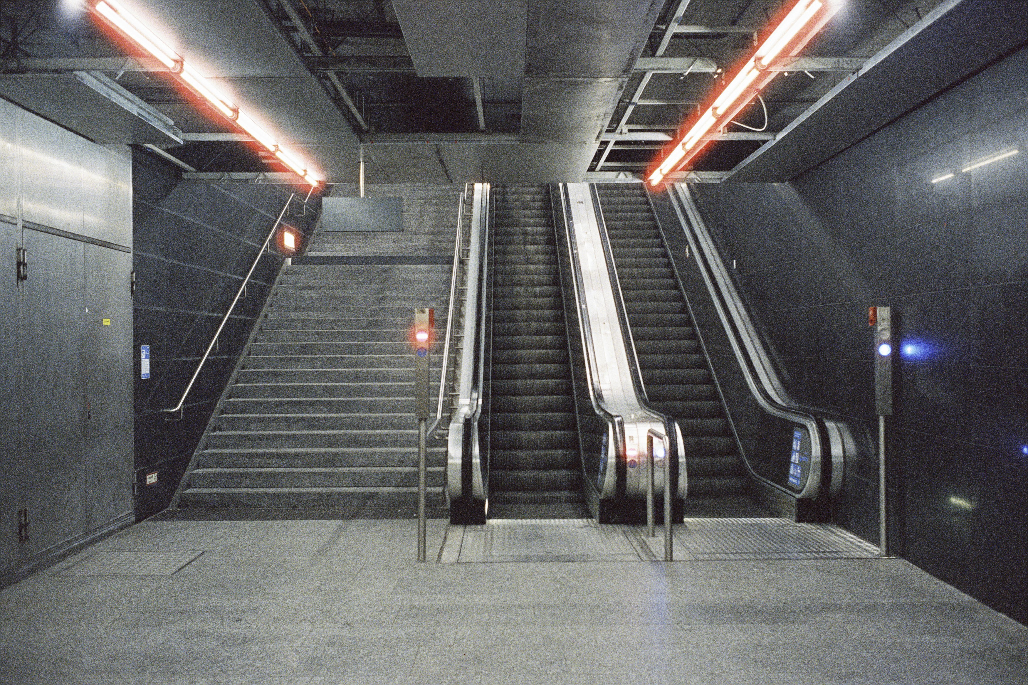 an escalator in a subway station with two escalators, Munich U-Bahn Underground Subway Tram Metro – Leica M6 (1987), Summilux-M 1.4 35mm (1983). Hi-Res analog scan by www.urbanfilmlab.com – CineStill Xpro 800 Tungsten