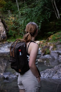 a woman with a backpack standing in front of a stream