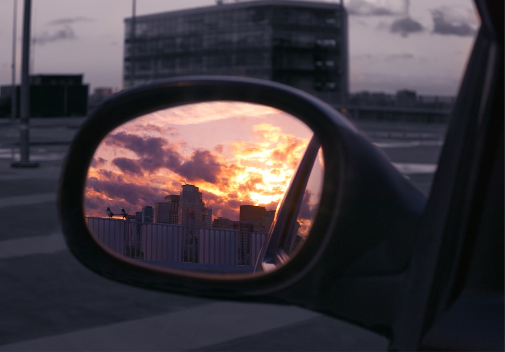 a rear view mirror reflecting a sunset in a city