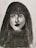 A monochrome charcoal portrait of a woman with long hair and bangs. The shading highlights her facial features such as the eyes, nose, and lips, giving depth and intensity to the portrait.