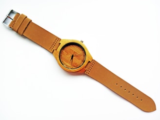 A minimalist wristwatch with a leather strap resting on a wooden table.