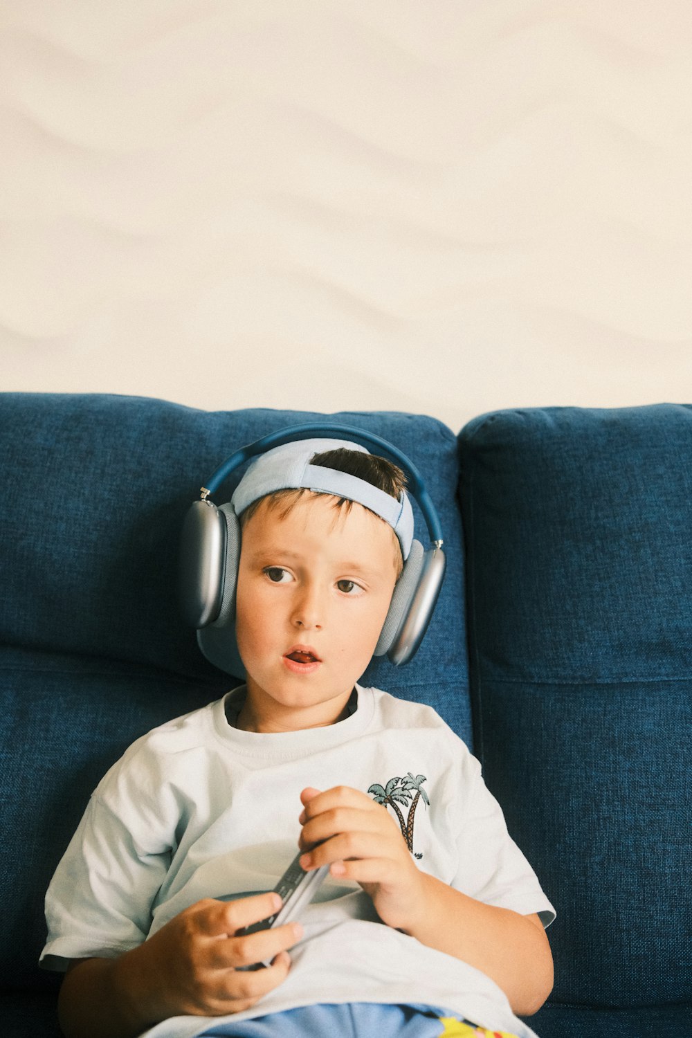 a young boy sitting on a blue couch wearing headphones