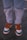 Worn and slightly torn light blue jeans with the phrases 'DON'T WORRY' and 'BE HAPPY' printed near the knees. The jeans are paired with colorful sneakers featuring green, orange, and white colors. The laces are bright orange, and the background appears to be a rough, textured ground surface.