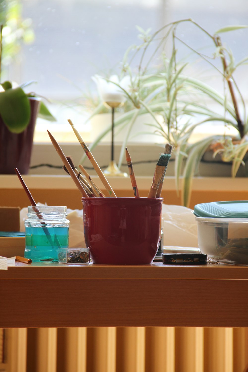 a wooden table topped with a cup filled with paint and brushes