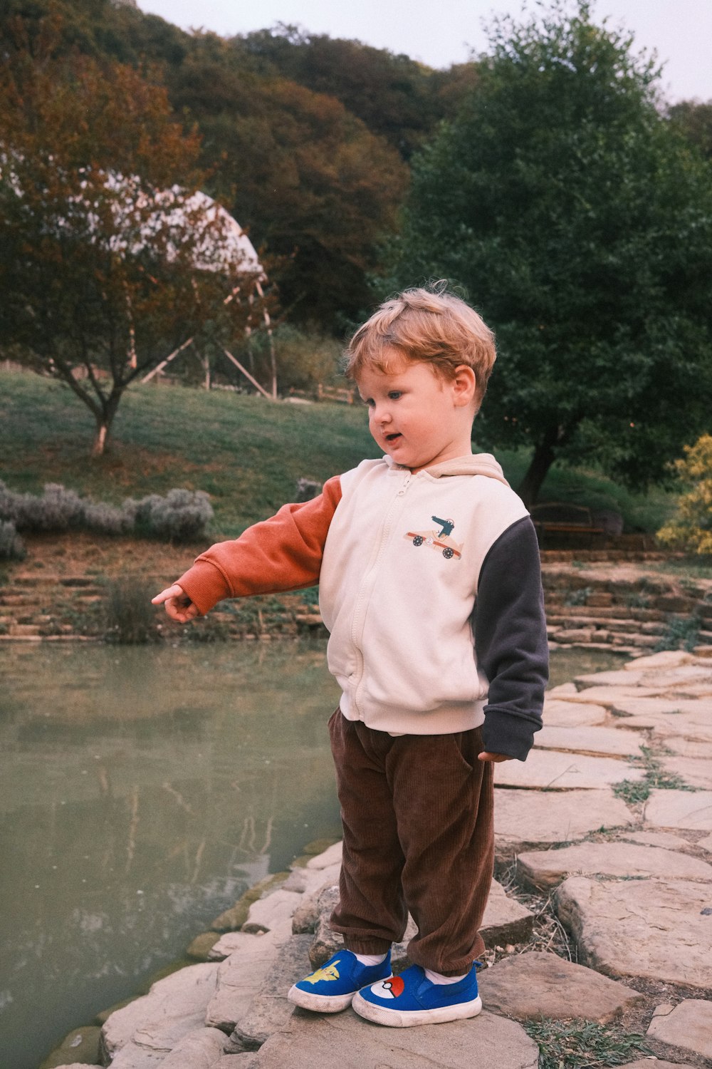 a young boy standing on a stone walkway next to a pond
