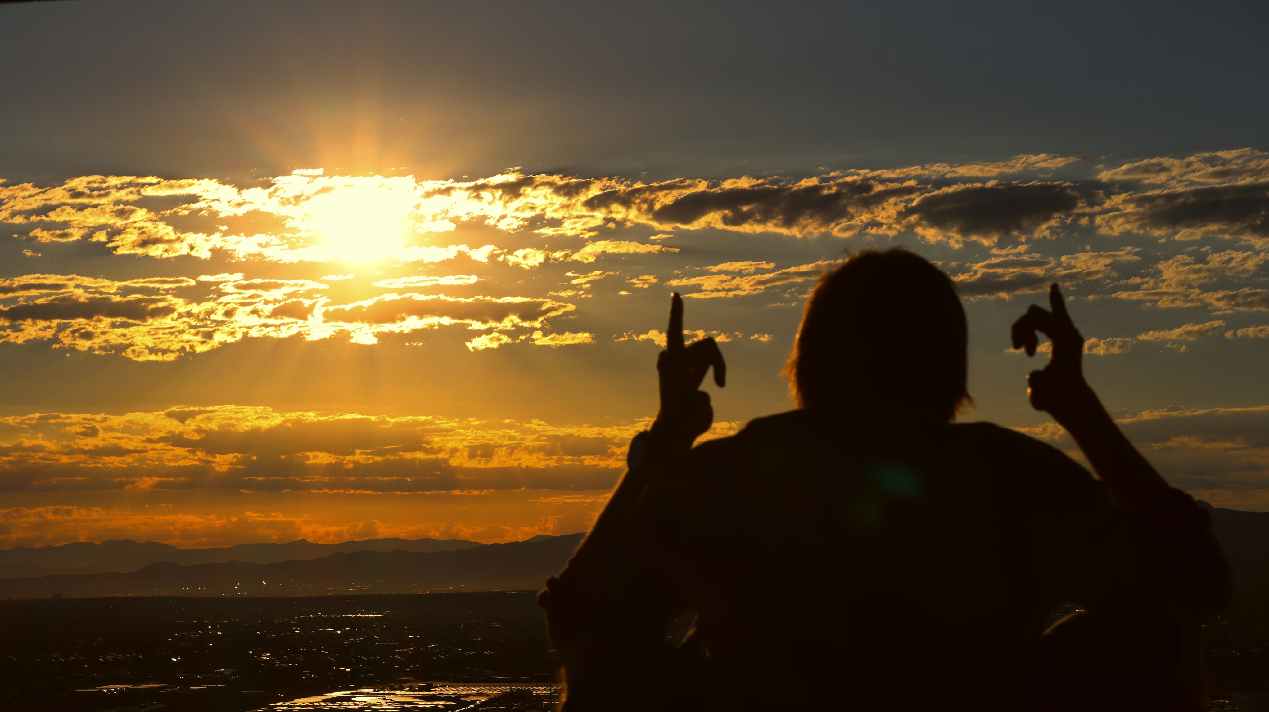 Person with hands raised in worship at sunset, silhouette against vibrant orange and purple sky