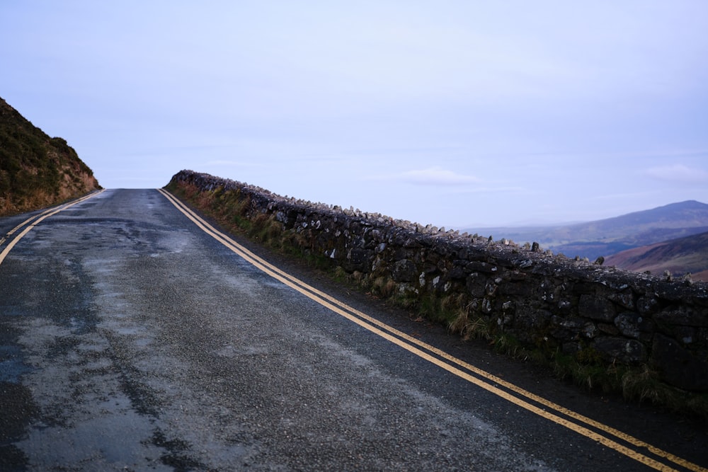 an empty road with a stone wall on the side
