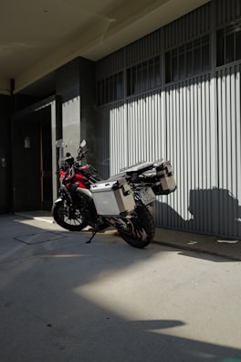 A motorcycle parked outside a modern office building with delivery boxes.