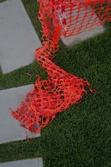 Bright orange construction netting is spread across a grassy area and partially over concrete paving stones, appearing slightly tangled.