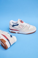 A pair of beige athletic shoes with white laces and blue and red accents. The shoes feature a noticeable logo on the side and are set against a solid blue background.