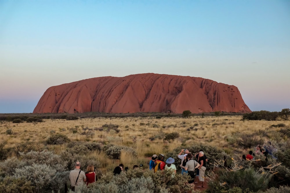 a group of people standing in front of a large rock