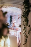 A beautifully decorated indoor space features a three-tiered cake surrounded by floral arrangements and adorned with lights. The setting includes intricate lattice work and is adorned with greenery, creating an elegant and festive atmosphere.