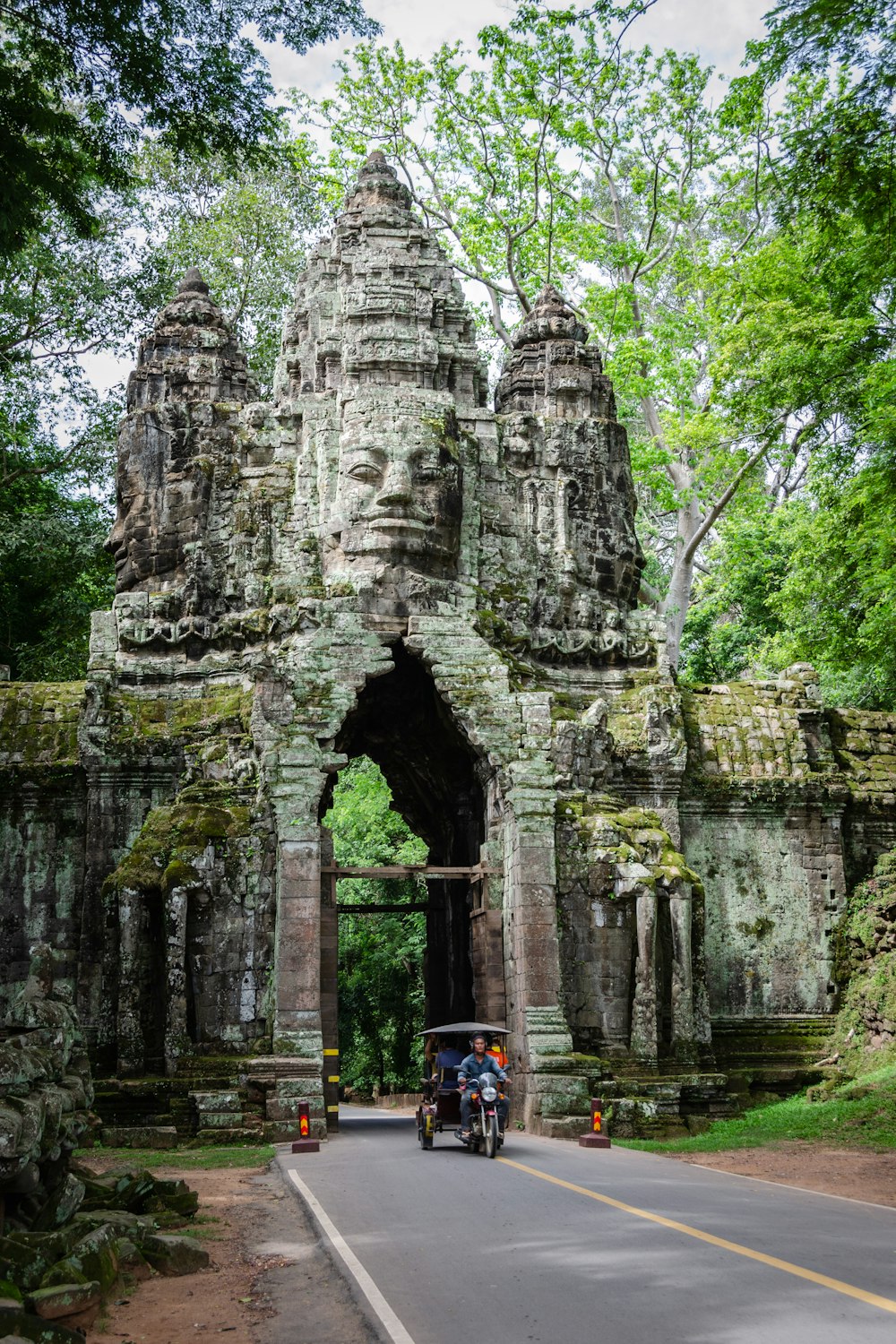 a motorcycle driving down a road next to a stone structure